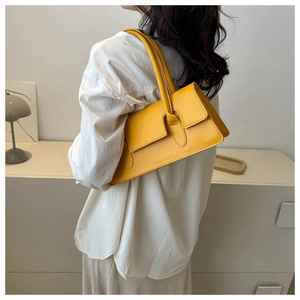 Side view of a structured mustard yellow underarm bag worn by a model in soft light