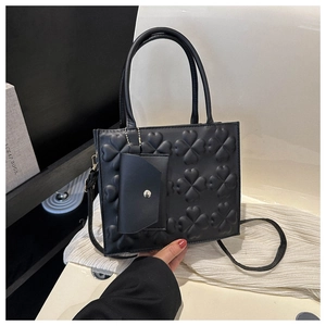 Detail of black faux leather handbag with embossed clover patterns and mini envelope charm