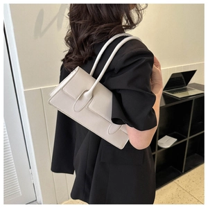 Detailed shoulder view of a minimalist cream baguette bag paired with a black blazer