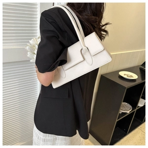 Close-up of a white leather baguette shoulder bag worn by a model in a minimalist setting