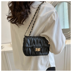 Detail of black quilted crossbody bag with gold chain strap worn by a female model