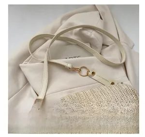 Détail du sac en paille tressée avec chaîne fleur dorée et bandoulière sur tissu