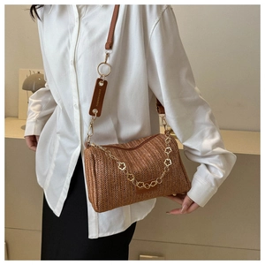 Détail d'un sac seau tressé marron avec chaîne à fleurs dorées et étiquette de mode