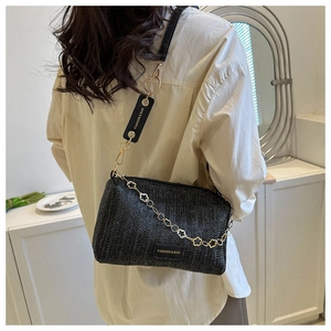Détail du sac à bandoulière noir tissé avec chaîne trèfle dorée et sangle réglable