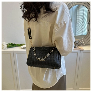 Détail du sac bandoulière tissé noir avec chaîne florale dorée et étiquette chic