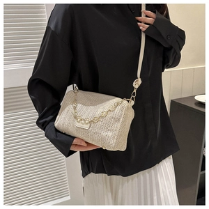 Détail du sac bandoulière en paille tressée avec chaîne fleurie dorée et texture ondulée