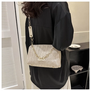 Détail du sac bandoulière tissé beige avec chaîne fleurie dorée et large bandoulière