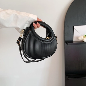 Retro black crescent handbag with pleated texture and round handle held by a hand