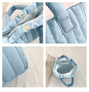 Detail view of light blue puffer tote bag featuring vertical quilting and gold magnetic clasp