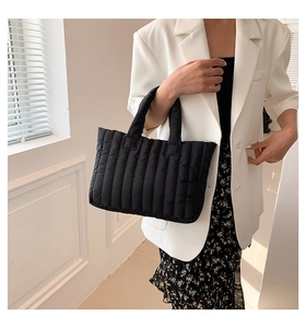 Close-up of black quilted puffer tote bag with glossy finish held by a model in a white suit