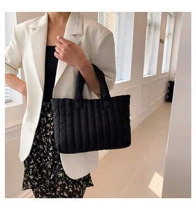 Chic black quilted tote bag held by a model in a stylish white blazer and floral dress