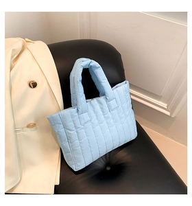 Detail of light blue quilted tote bag with vertical stitching on black leather chair