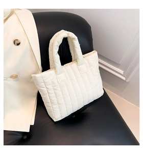 Detail of white quilted tote bag with padded handles on a black leather chair background