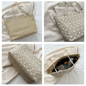 Dettagli di una borsa tote in paglia beige con ricami floreali bianchi e tracolla dorata