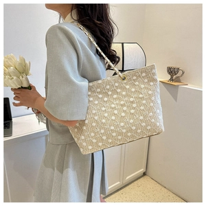 Dettaglio borsa tote in paglia con decorazioni floreali in pizzo e catena dorata
