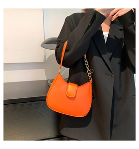 Détail d'un sac hobo orange vif avec chaîne dorée sur un mannequin en blazer noir