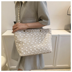 Dettaglio di ricamo floreale su borsa tote in paglia beige con tracolla a catena