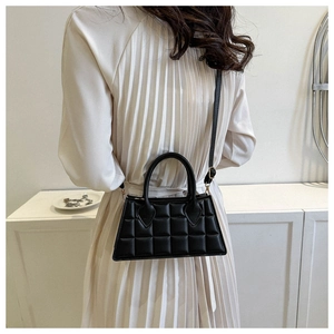 Détail du sac bandoulière noir matelassé porté par un mannequin en robe élégante