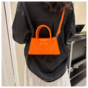 Sac bandoulière matelassé orange vif porté sur une tenue noire pour un beau contraste