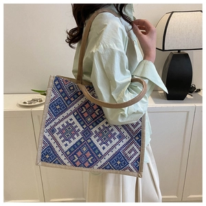 Detail of colorful geometric woven tote bag with thick braided handles on model shoulder