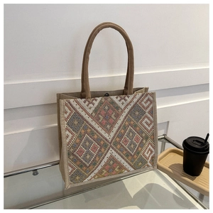 Close-up of ethnic tote bag with geometric woven patterns and jute handles on glass table
