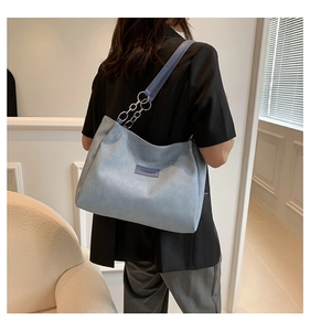 Detail of the blue suede tote bag showing its metal chain strap and brand leather patch