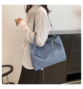 Side view of a blue retro tote bag with silver chain worn with a professional outfit