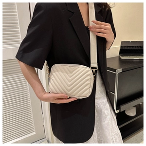 Close-up of cream quilted crossbody bag with V-shaped stitching and wide strap on model