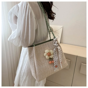 Detail of straw woven tote bag with green straps floral pendant and decorative silk scarf