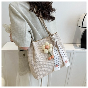 Detail of woven beige tote bag with a floral charm and geometric silk scarf handle