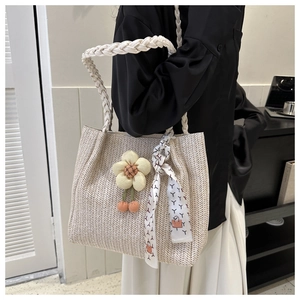 Detail of woven straw tote bag featuring decorative floral charms and silk scarf handle