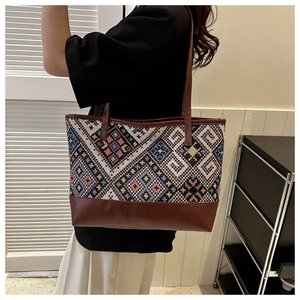 Detail of large geometric jacquard tote bag with brown leather trim worn on shoulder