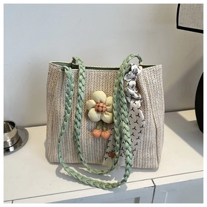 Detail of beige woven tote bag featuring green straps and decorative floral pendants