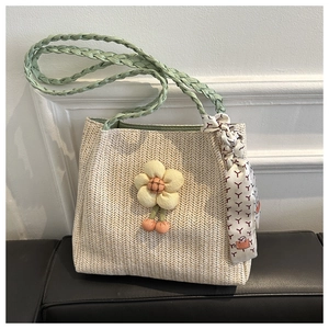 Detail of straw woven tote bag with green braided handle, flower decor, and silk scarf