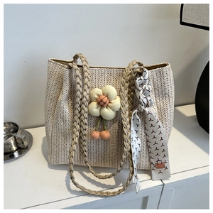 Detail of straw tote bag featuring a woven handle, fabric flower, and printed silk scarf