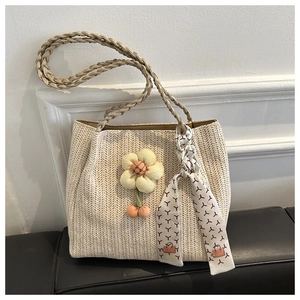 Close-up of beige straw tote bag with woven V-pattern and decorative floral pendant
