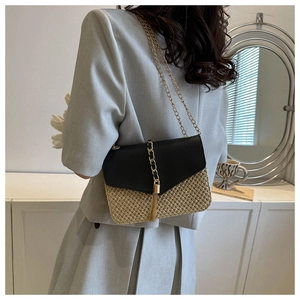 Detail shot of straw crossbody bag with black leather flap and gold chain strap on model