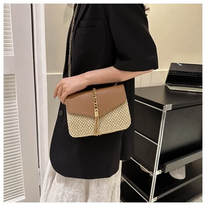 Detail of straw woven crossbody bag with brown leather flap and golden fringe accent