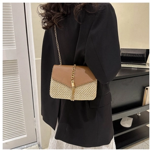 Detail of straw woven crossbody bag with brown leather flap and gold chain fringe