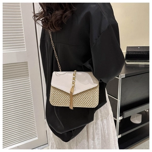 Detail of straw woven crossbody bag with beige leather flap and gold tassel accent