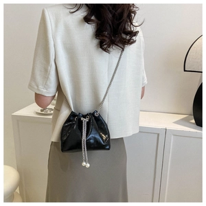 Detail of black drawstring bucket bag with silver chain strap and pearl accents