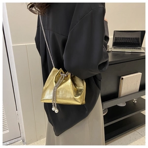 Detail of gold bucket bag with crocodile texture, chain strap, and pearl drawstring detail