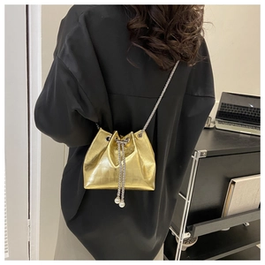 Detail of golden crocodile pattern bucket bag featuring pearl charms and chain drawstring