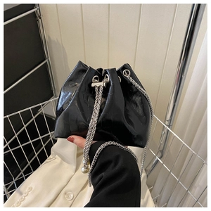 Detail of a black faux crocodile bucket bag featuring silver chains and pearl accents