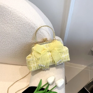 Elegant yellow tweed handbag with mesh bow and pearls on a white textured chair