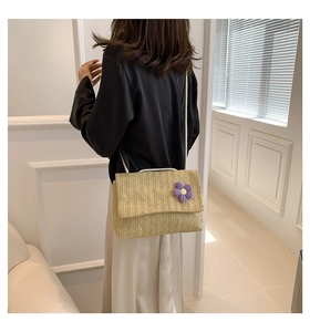 Dettaglio della borsa a tracolla in paglia con fiore in maglia viola indossata dal modello