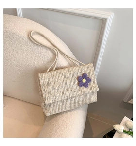 Dettaglio borsa di paglia beige con fiore viola lavorato a maglia su divano bianco