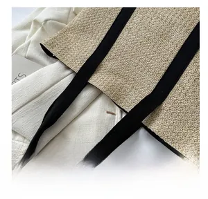 Detailed top view of beige woven tote bag with black canvas straps and a fashion magazine