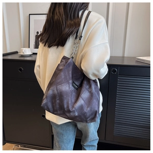 Detail of grey quilted tote bag with silver chain strap and fashion label on shoulder