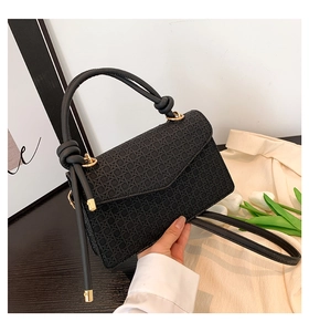 Détail d'un sac bandoulière noir avec gaufrage géométrique et garniture dorée